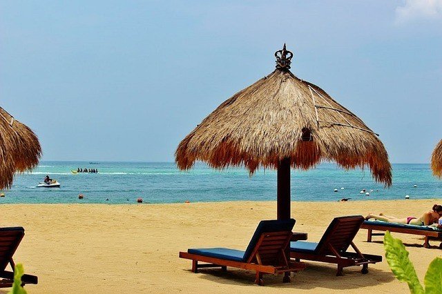 A beach with lounge chairs and thatched umbrellas.