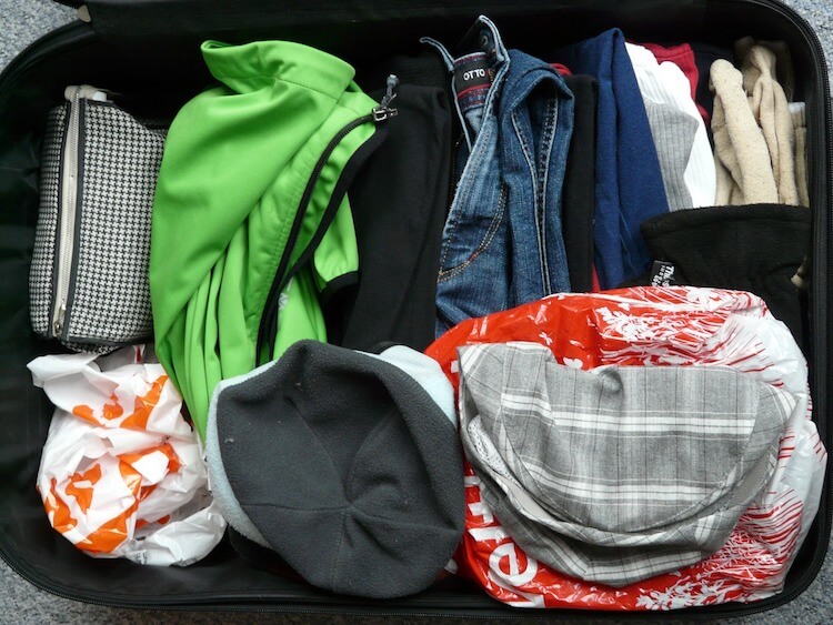 Open suitcase packed with a variety of clothes, including jeans, shirts, and a green jacket, neatly arranged to optimize space.