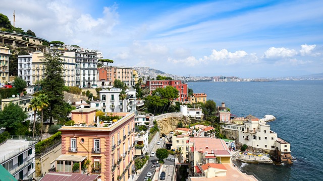 Coastal cityscape with densely packed historical buildings overlooking a calm sea under a partly cloudy sky.
