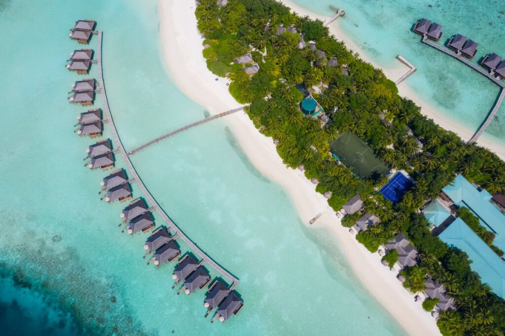 Arial view of an island with overwater bungalows on two sides.