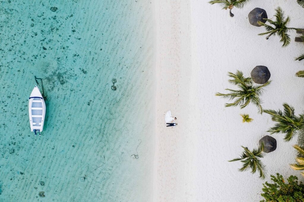 Mauritius beach with white sand, thatched umbrellas, and a couple dressed in wedding attire.